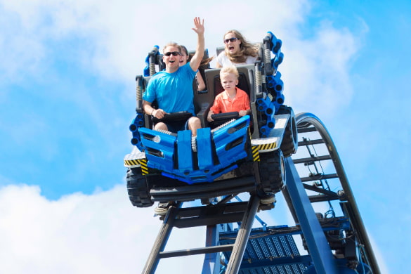 a family on a roller coaster screams as it begins its descent down a big hill