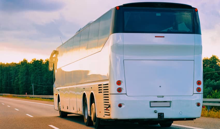 A plain white full size charter bus driving on a road