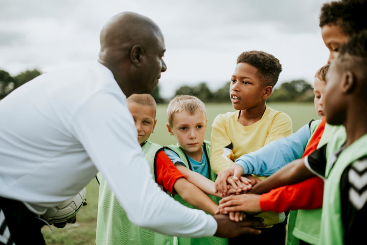 members of a young sports team put their arms in with their coach