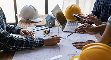 Construction workers gather around a table with hardhats and plans